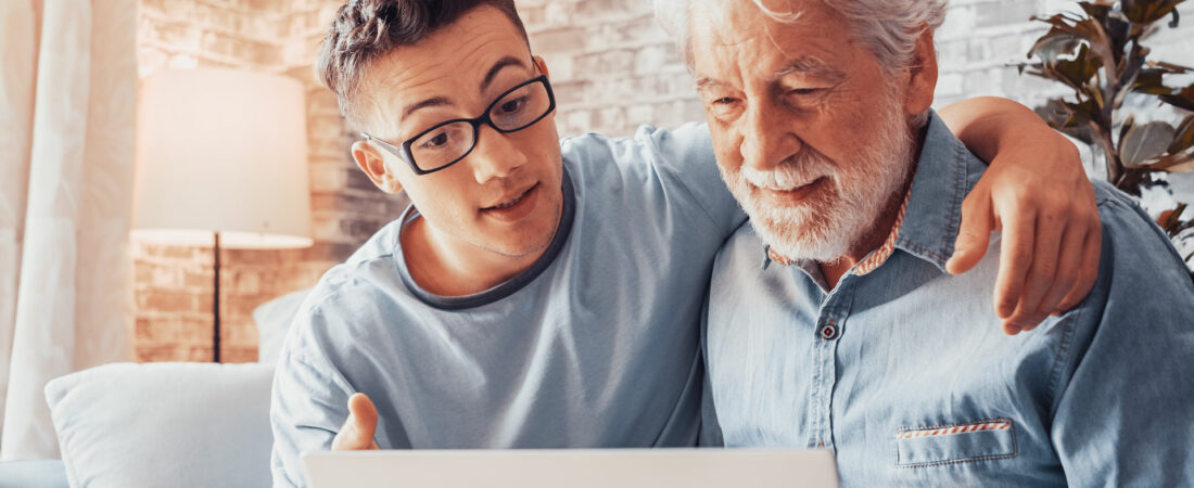 A young man with glasses helping an older man use a technical device.
